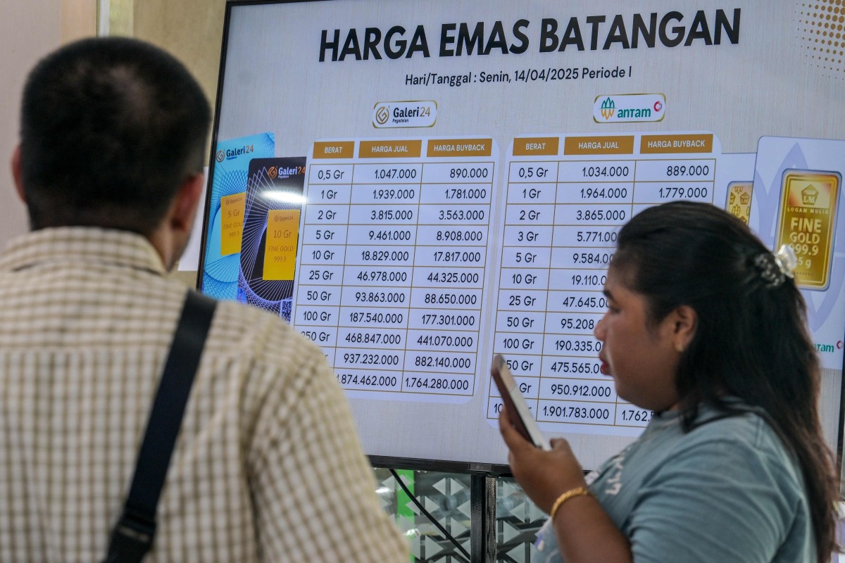 A customer uses her smartphone while conducting a gold transaction as a monitor displays the gold price per gram at Galeri 24 owned by Pegadaian, state owned pawnshop, in Jakarta on April 14, 2025. (Photo by BAY ISMOYO / AFP)
